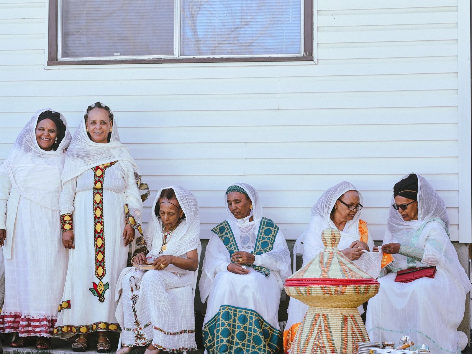 Group of women in white habesha dresses standing together outside a house