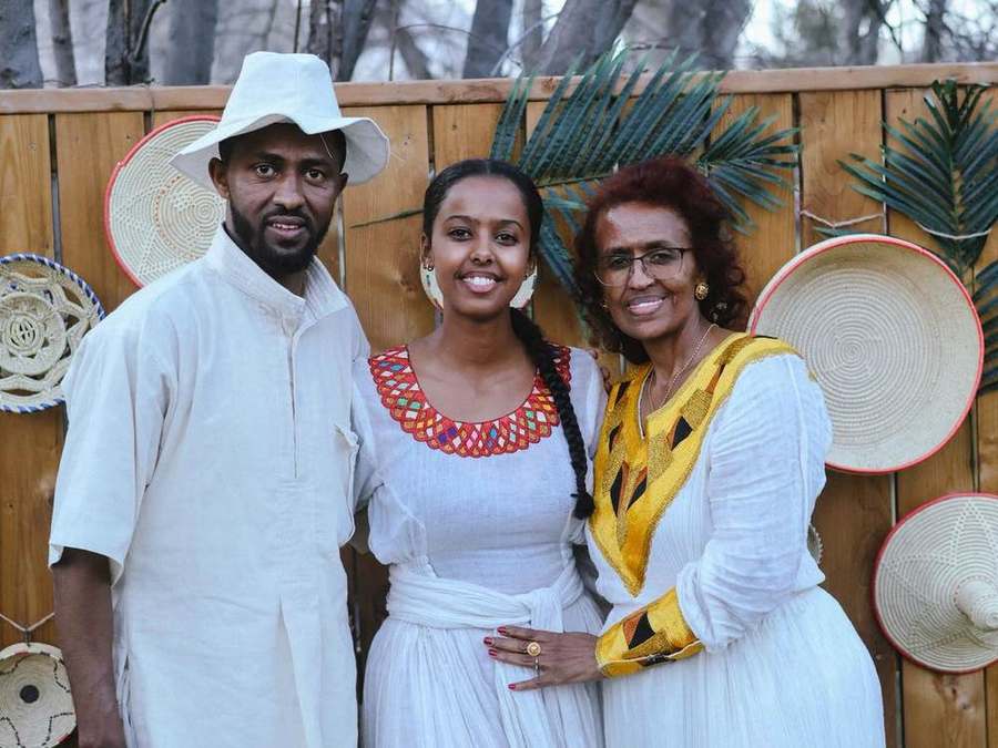 A family of three smiling together by the fence