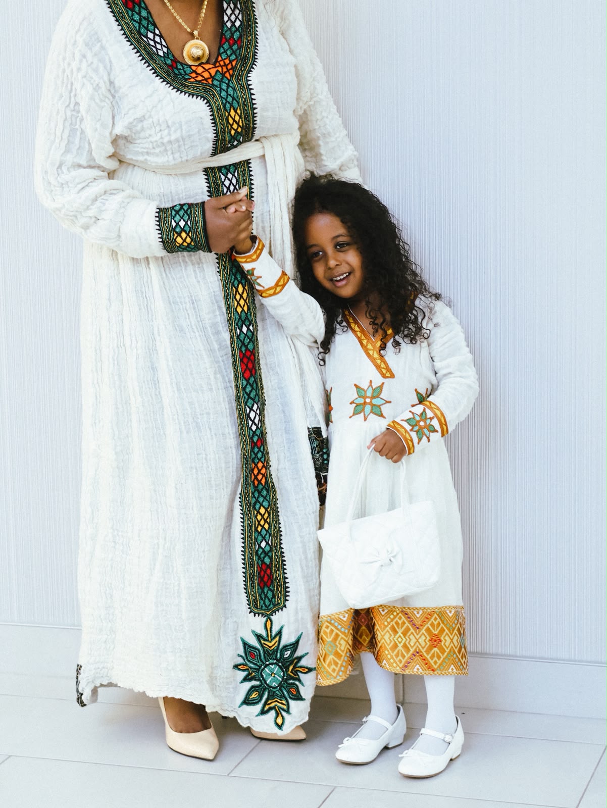 Mother and daughter holding hands, both in white embroidered dresses