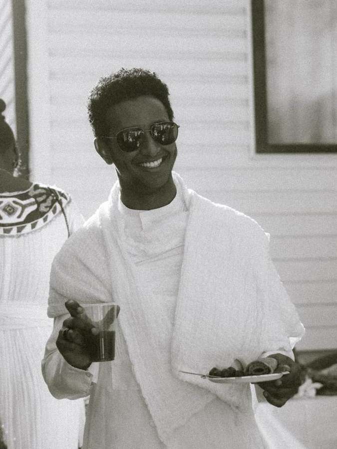 A man smiling, holding a drink and a plate of food