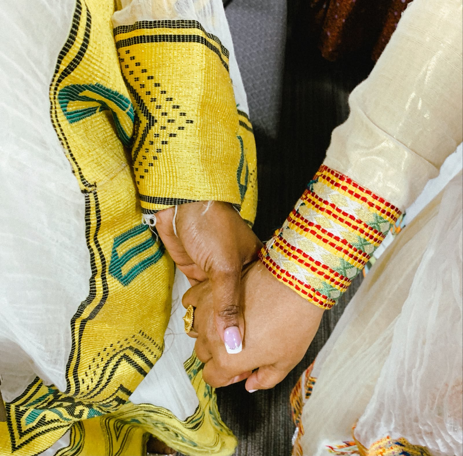 Bride and groom holding hands, wearing woven habesha clothing sleeves